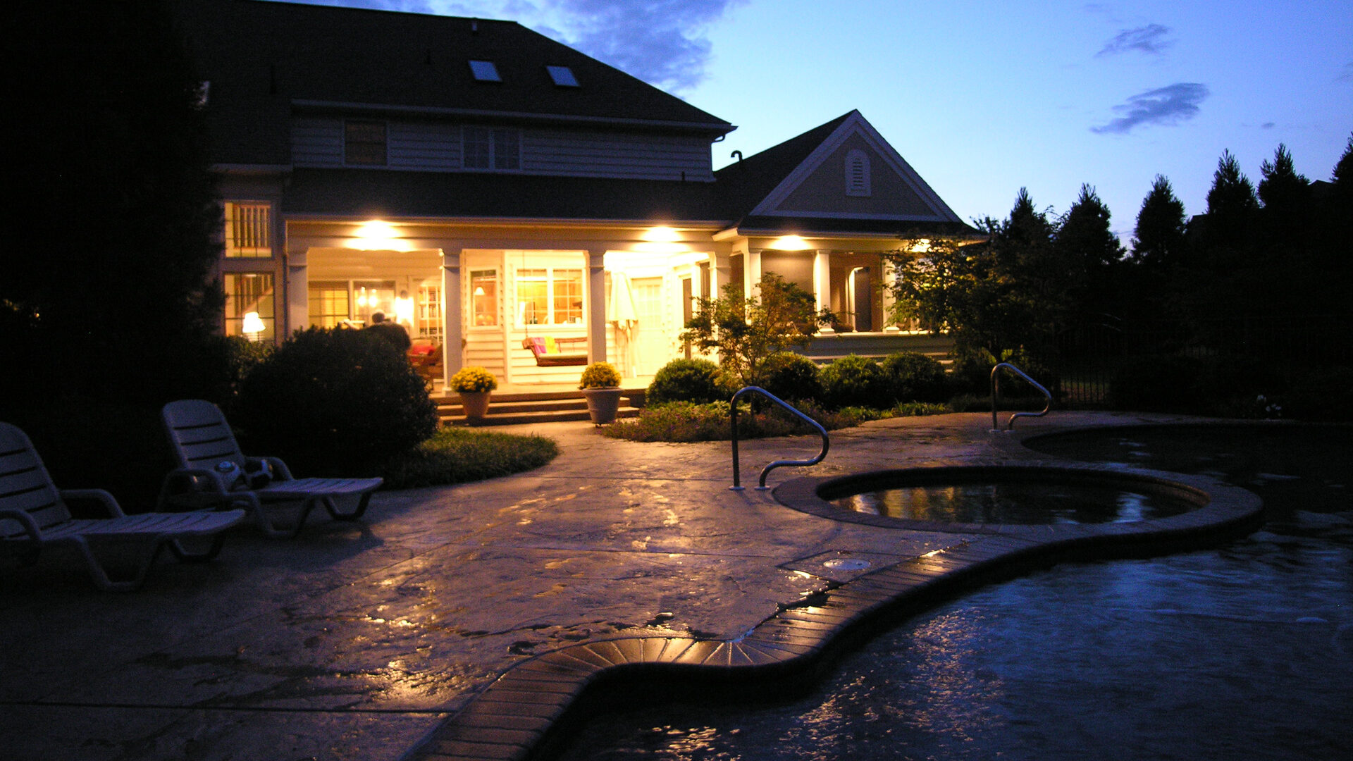 A Home'S Outdoor Patio Lights Showcasing Well-Trimmed Bushes, Trees And A Pool Designed And Installed By Hanselman Gardens