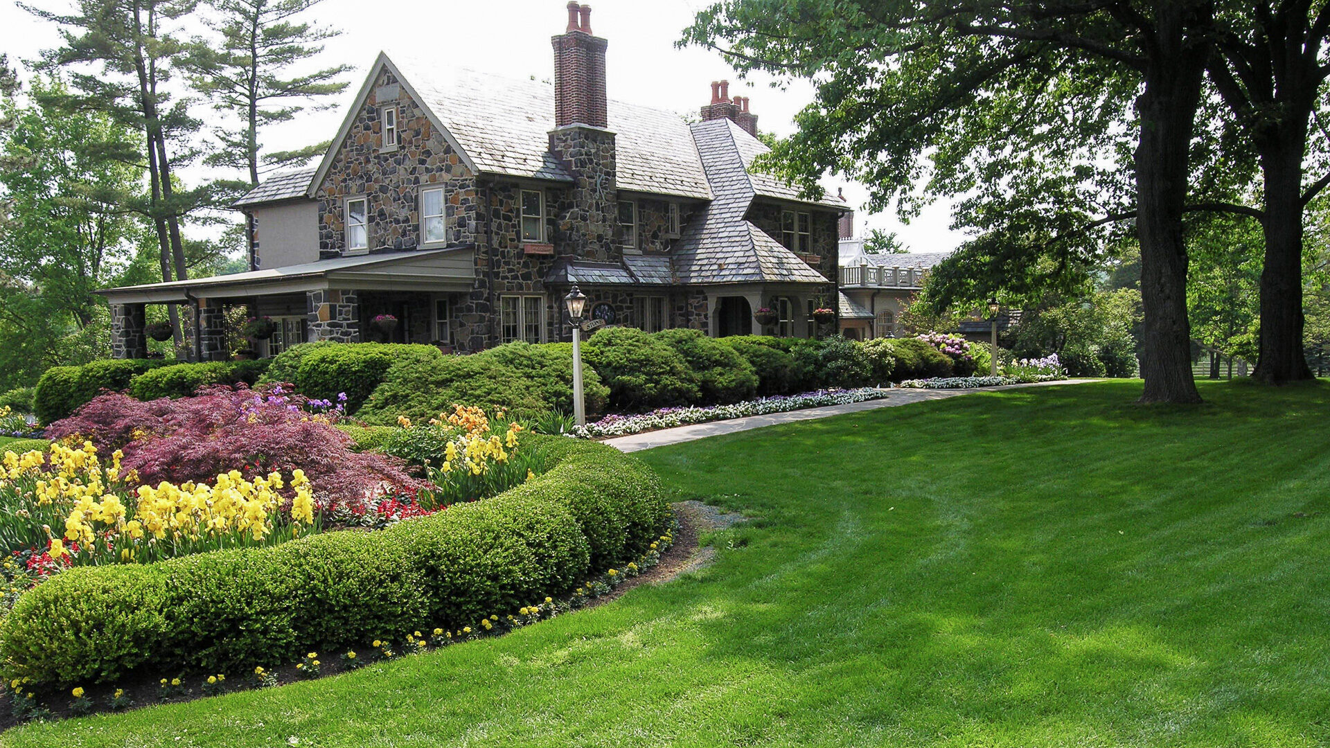 A Meticulously Maintained Lawn Surrounding A Charming Stone House, Its Vibrant Green Color Contrasting Beautifully With The Stone Facade