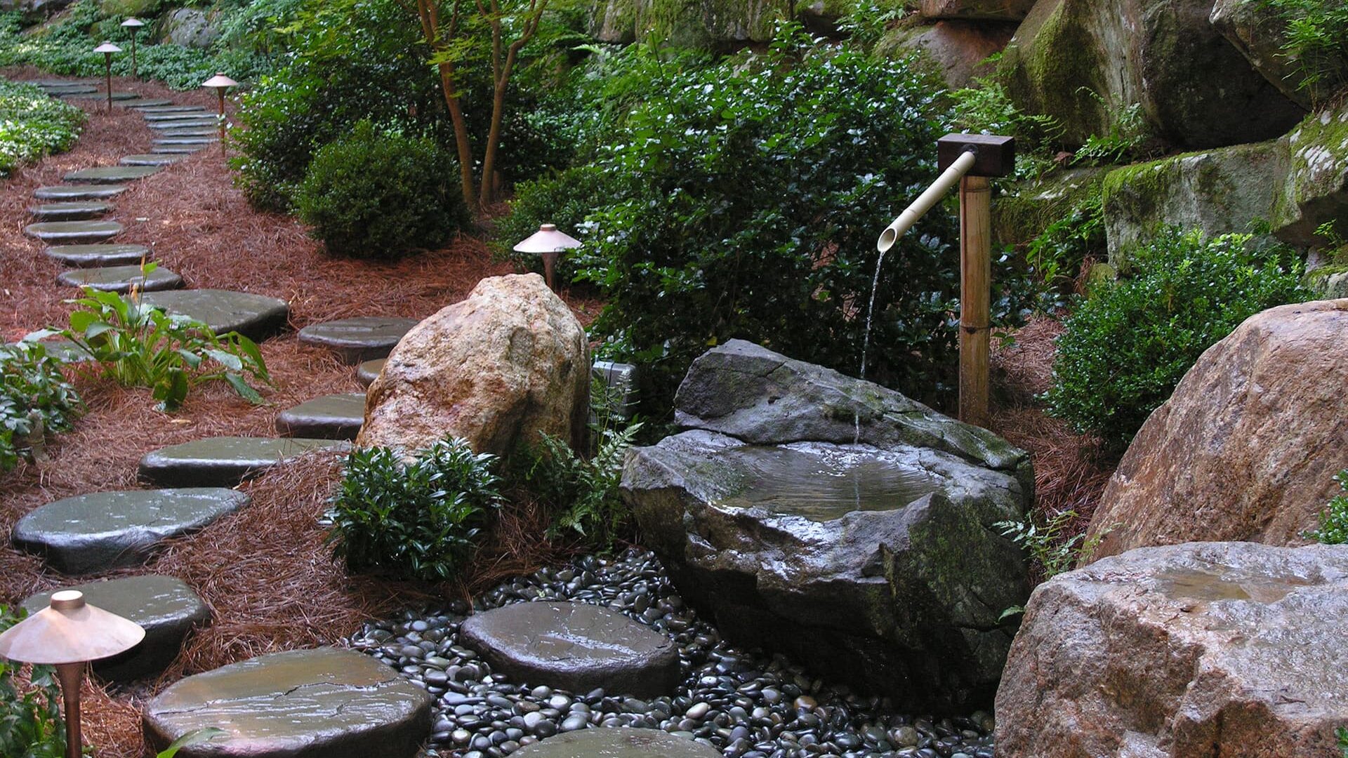 A Japanese-Inspired Backyard Garden Complete With Bushes, Stepstones And A Tsukubai Water Basin