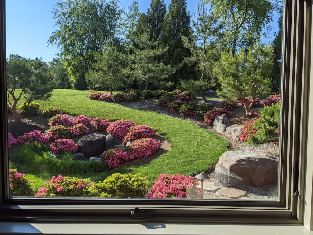 A Window View Of An Inside Out Garden Installed By Hanselman Gardens Across A Lush Green Landscape.